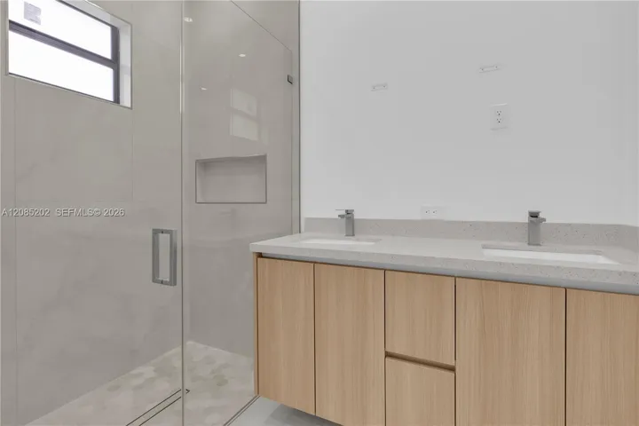 Double vanity featuring wood-finish cabinetry, stone-composite countertop with integrated dual sinks, and polished chrome faucets
