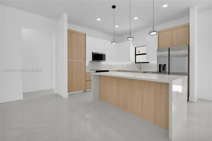 Kitchen featuring a central island with a stone-finish waterfall edge, two-tone cabinetry, stainless steel appliances, under-cabinet lighting, and recessed ceiling lights