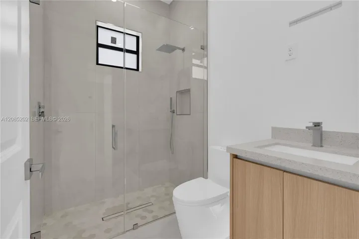 Walk-in shower with floor-to-ceiling tile, glass enclosure, rain-style shower head, and recessed wall niche
