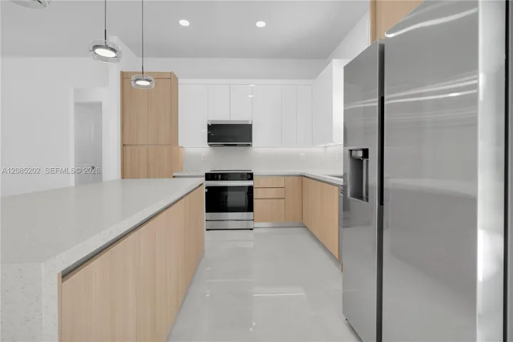 Kitchen featuring wood-finish lower cabinetry, white upper cabinets, stainless steel appliances, a large island with a composite countertop, and recessed lighting