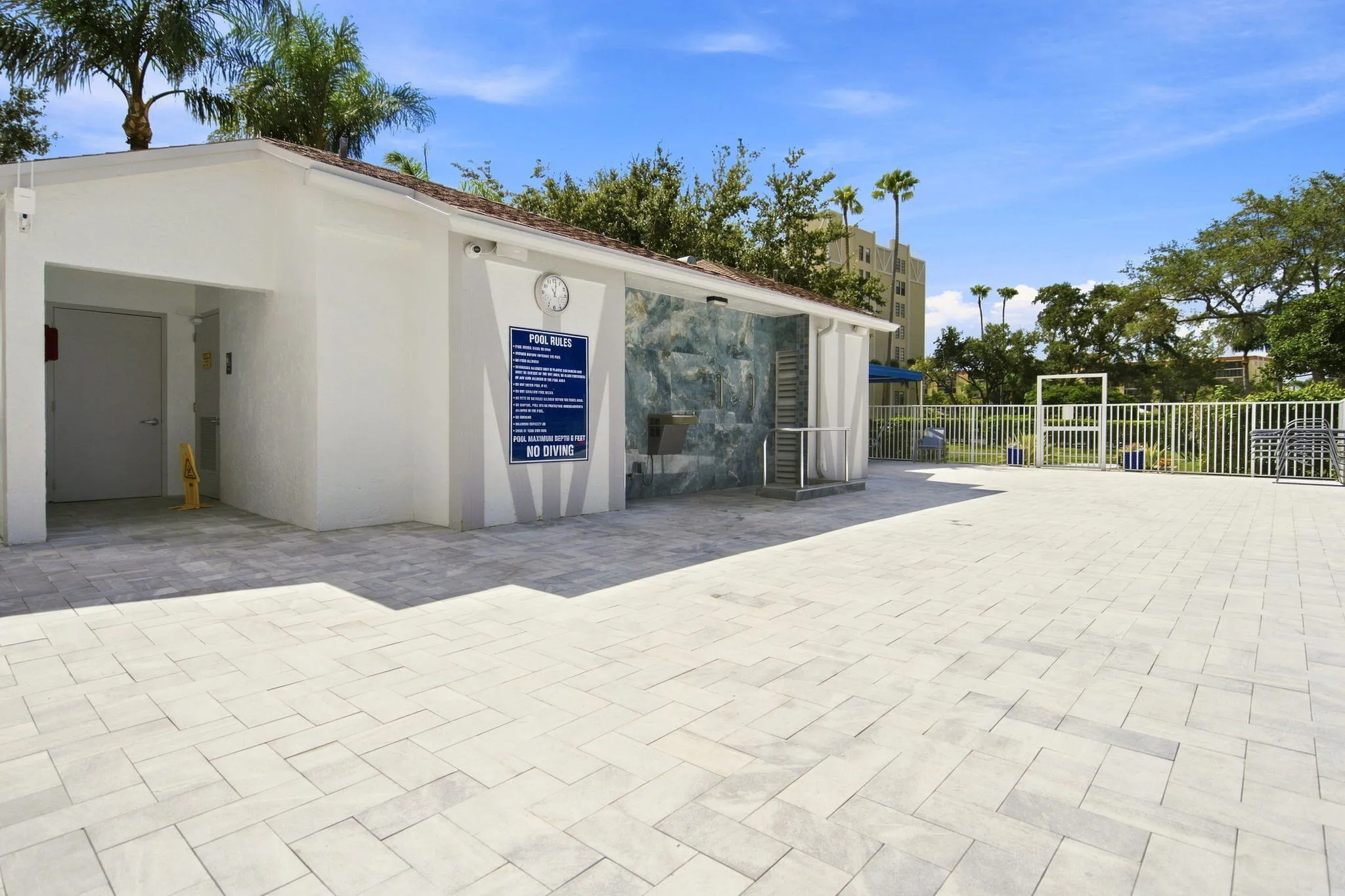 Open-air patio featuring paver flooring, a white stucco utility building with a tiled roof, and a white metal fence