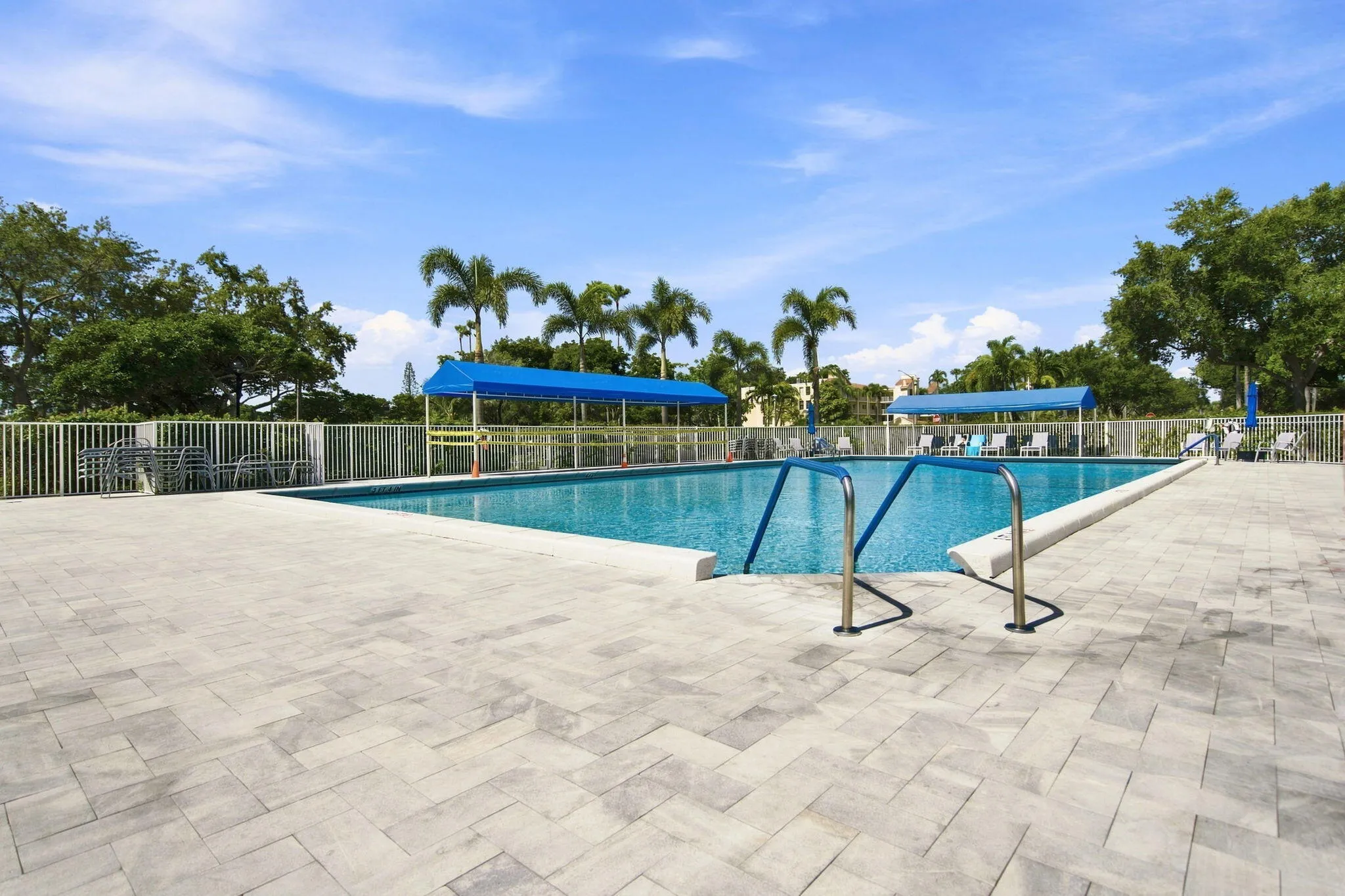 Expansive pool deck featuring light-toned paver flooring, a rectangular swimming pool, and a white perimeter fence