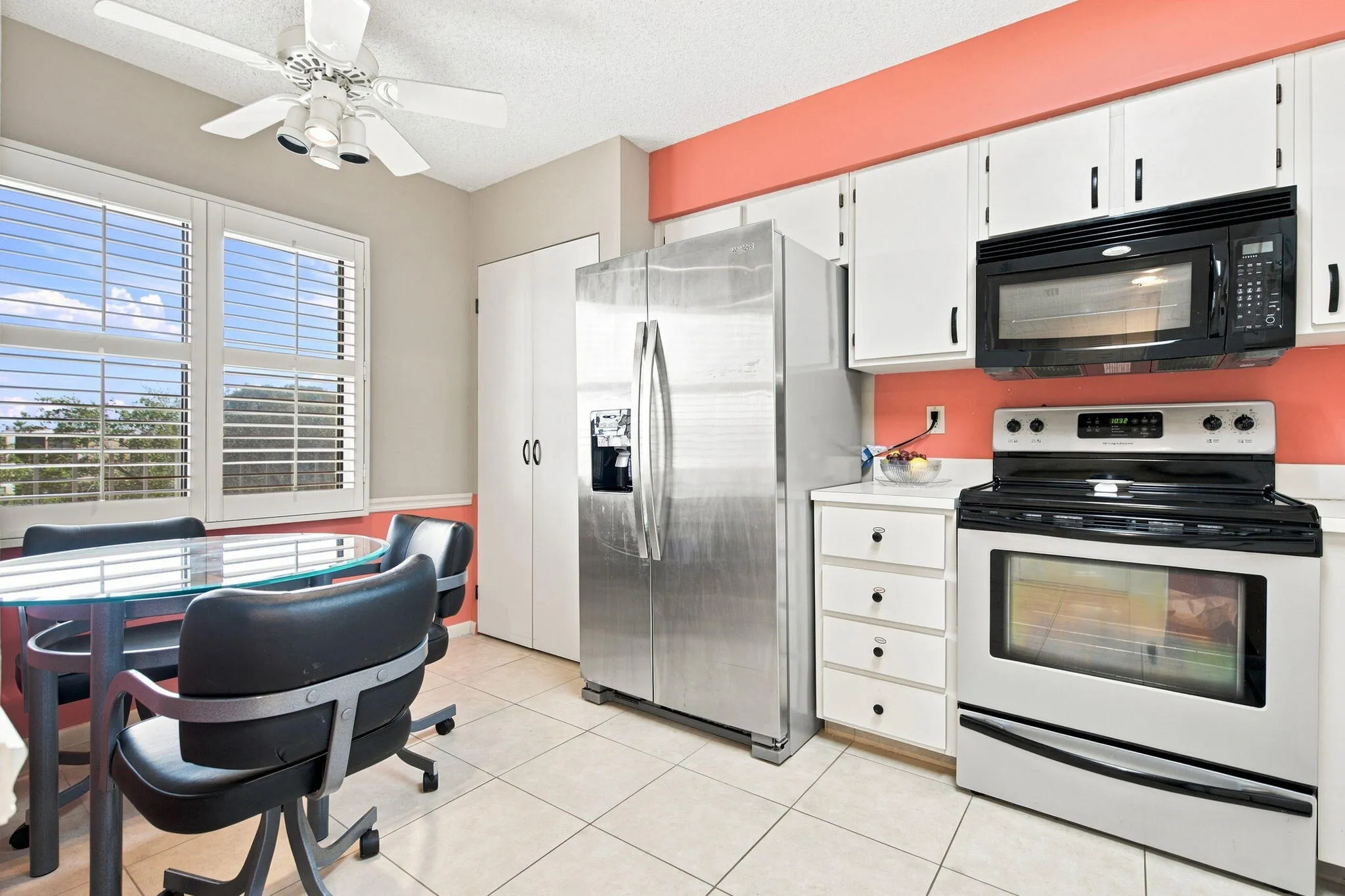 White tile flooring, white shaker-style cabinetry, stainless steel appliances, and white window shutters