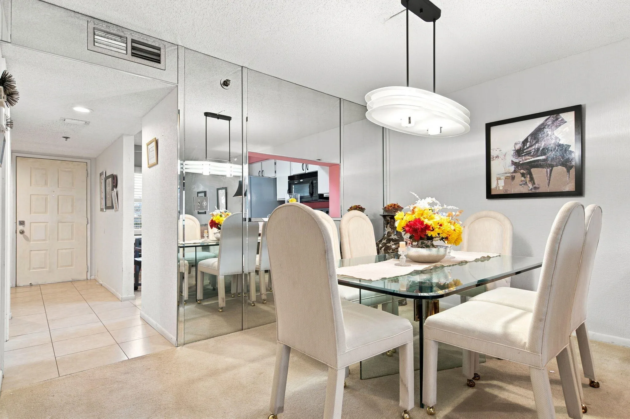 Contemporary overhead lighting fixture, full-height mirrored wall, tiled entry flooring, paneled entry door, and wall-mounted art