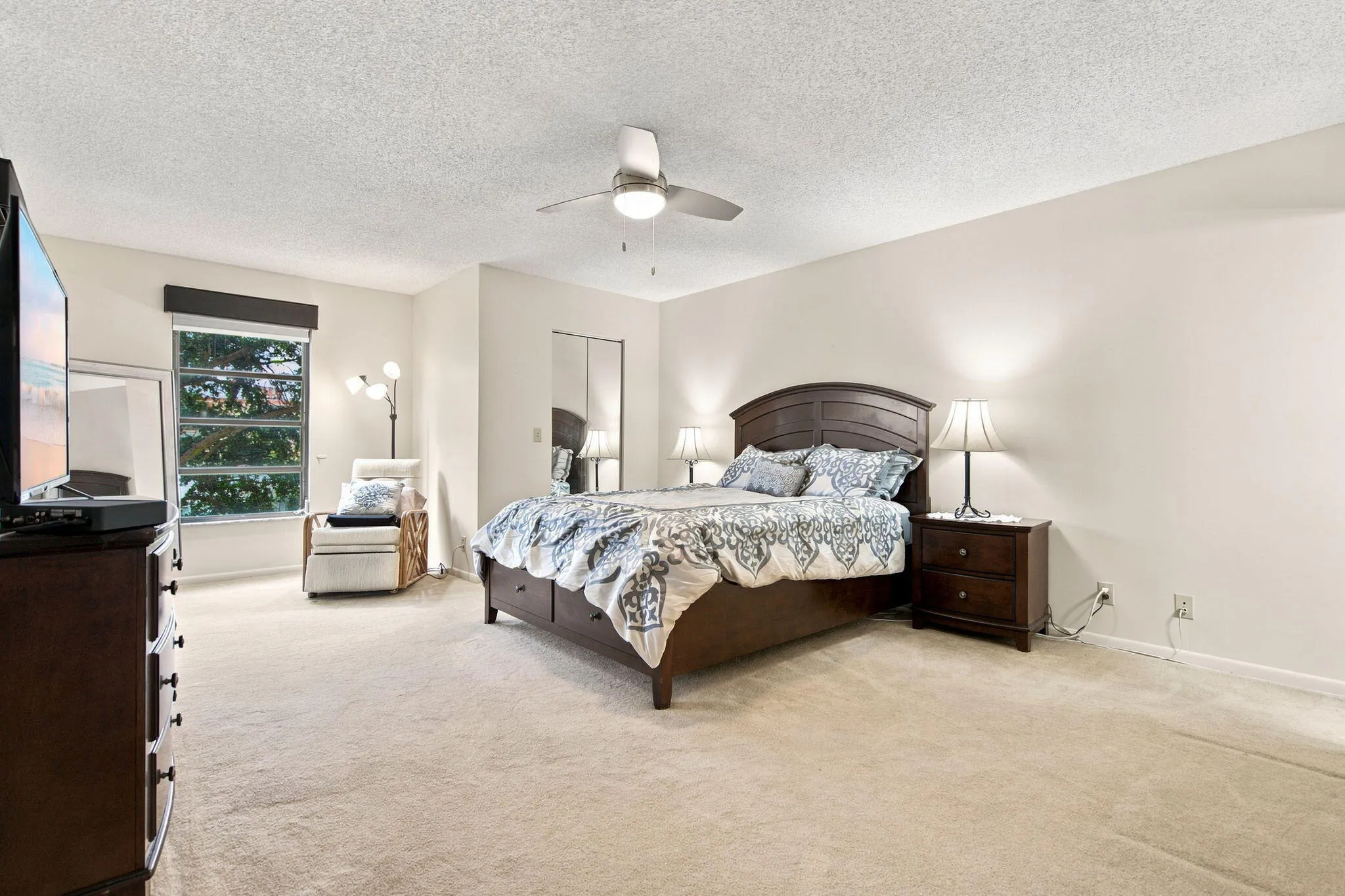 Carpeted bedroom featuring a ceiling fan with integrated lighting, a window with a valance, and mirrored closet doors