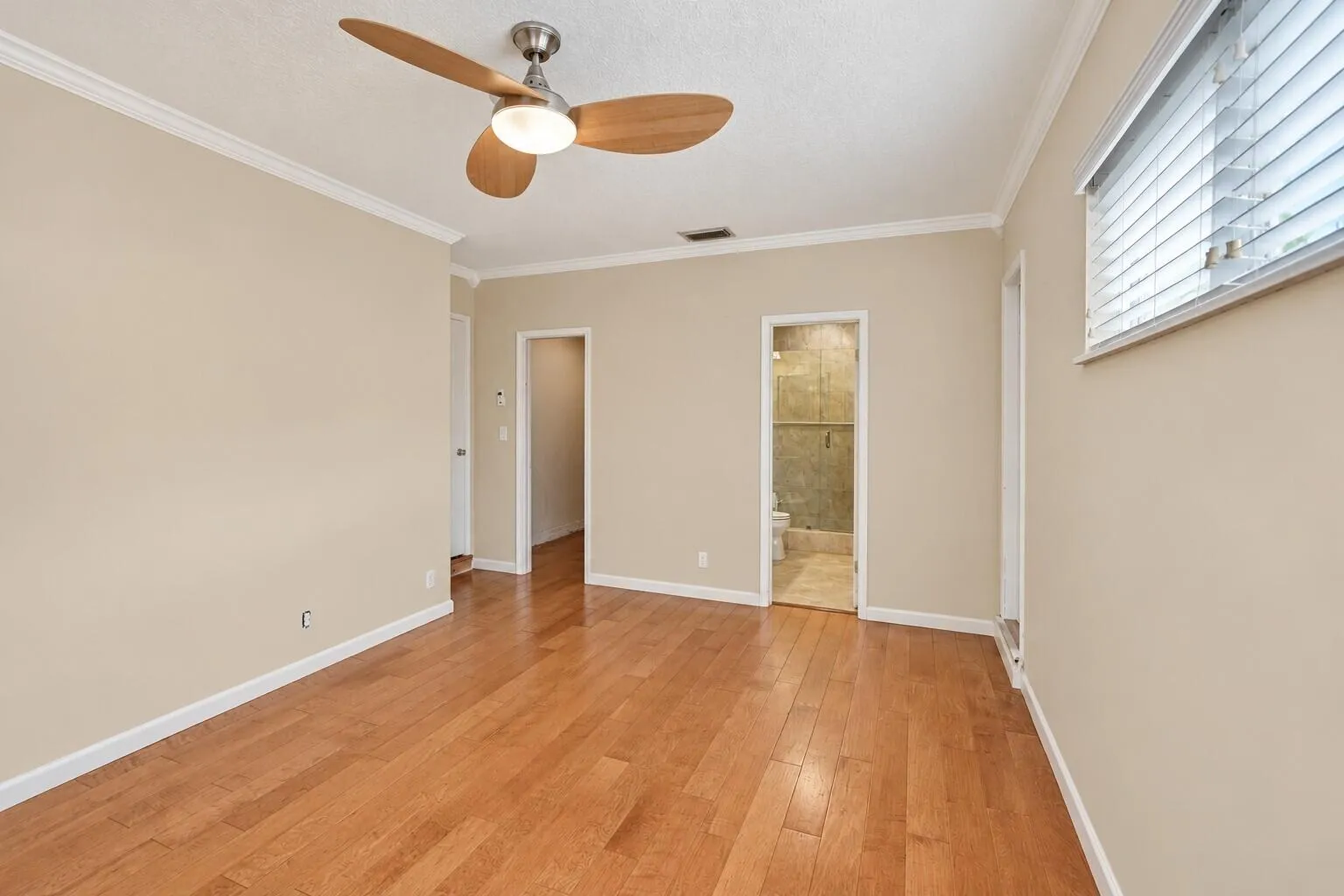 Wood-finish flooring with neutral wall tones, crown molding, and a ceiling fan with integrated lighting