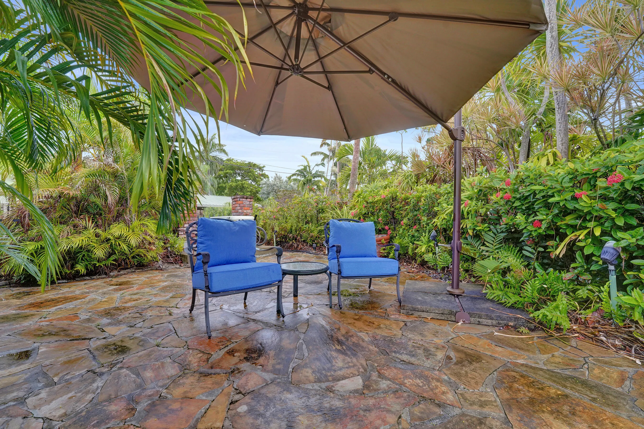 Stone patio with alcove sitting areas, an umbrella shade and lush tropical landscaping