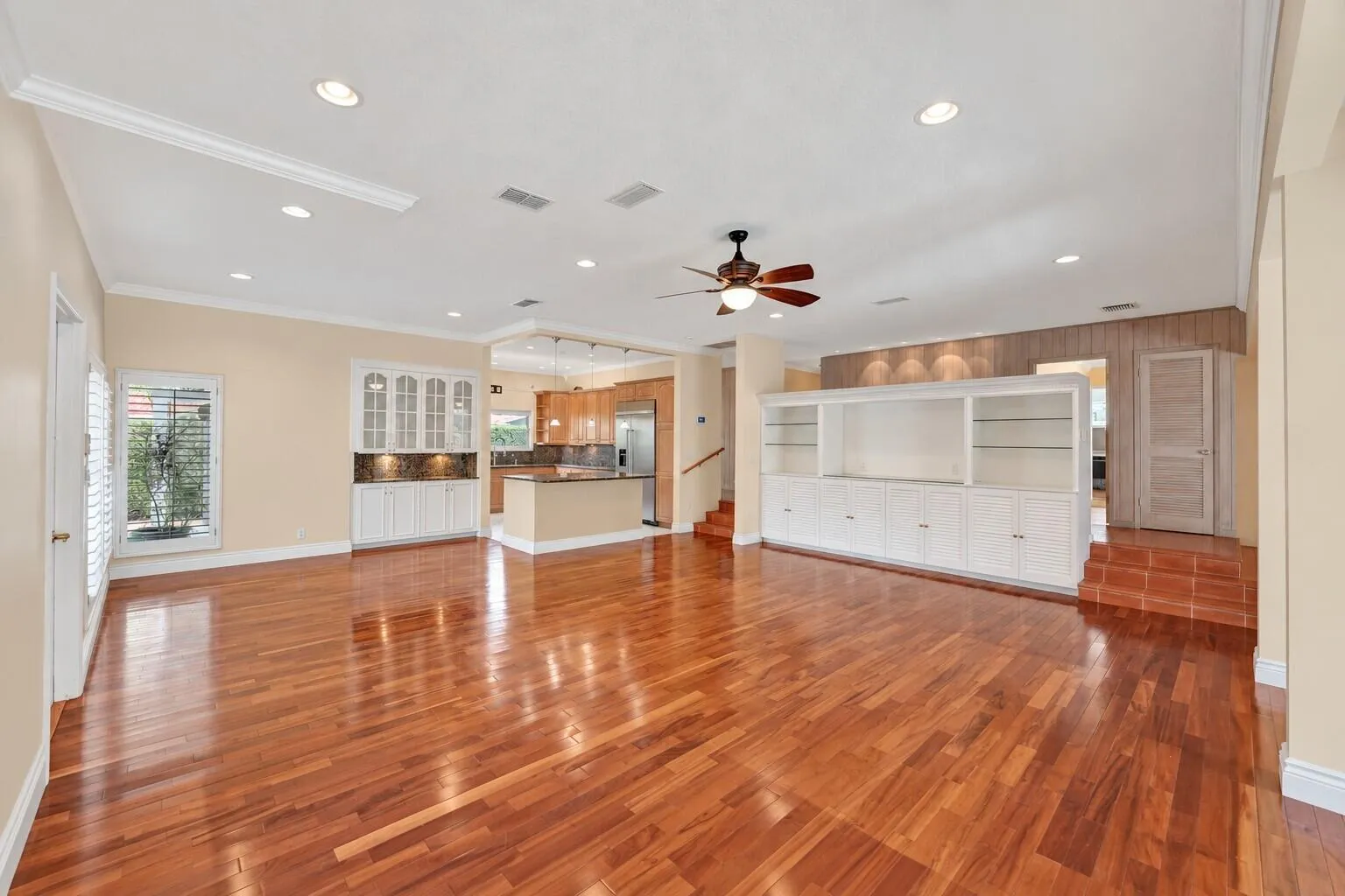 Expansive living area featuring hardwood flooring, recessed lighting, a ceiling fan, built-in cabinetry, and a dedicated kitchen space