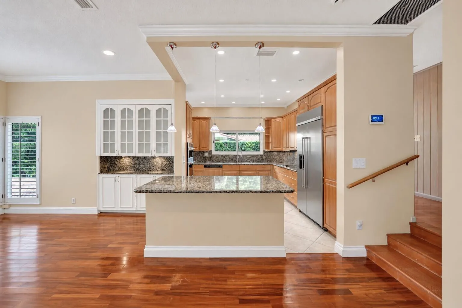 Wood-finish flooring throughout, kitchen with wood cabinetry and stainless steel appliances, breakfast bar with stone countertop, white built-in cabinetry with glass doors. Wall color has been virtually altered.