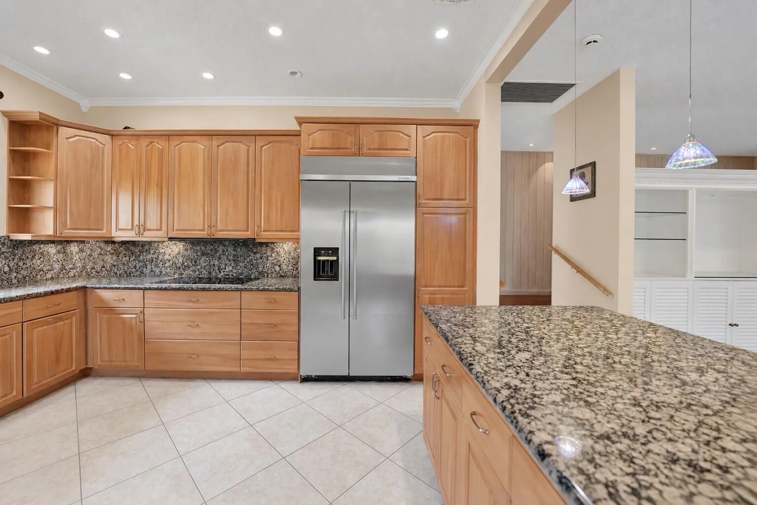 Kitchen featuring extensive wood cabinetry, stainless steel refrigerator, patterned stone countertops, recessed lighting, and tile flooring. Wall color has been virtually enhanced.