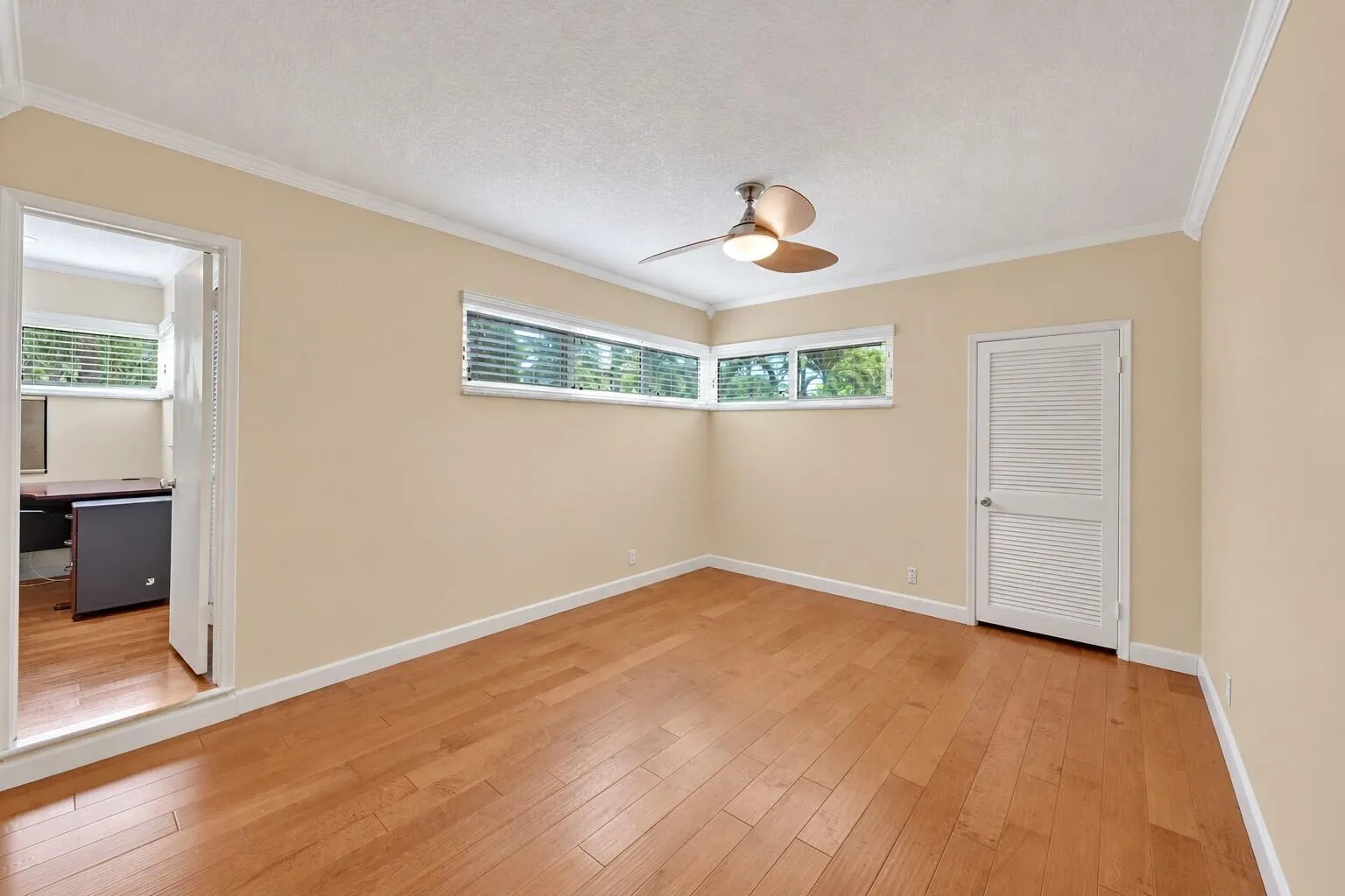 Wood-finish flooring with crown molding, transom-style windows, and a ceiling fan