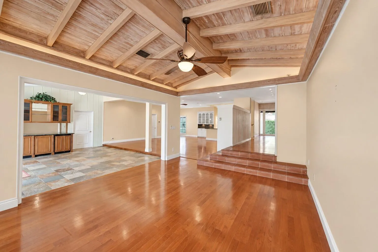 Vaulted wood-paneled ceiling with exposed beams, wood-finish flooring, built-in cabinetry, tiled floor section, and tiered tile steps