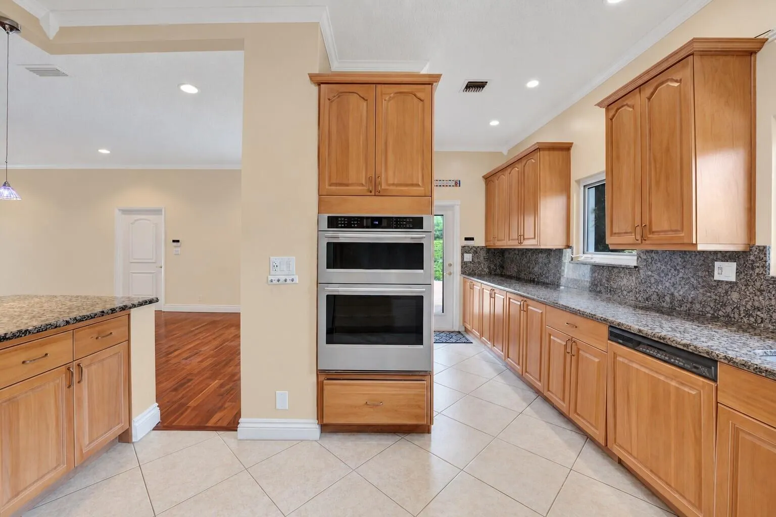 Kitchen featuring wood cabinetry, stainless steel double wall oven, neutral tile flooring, and dark speckled countertops. Wall color has been virtually enhanced. Wall color has been virtually enhanced.