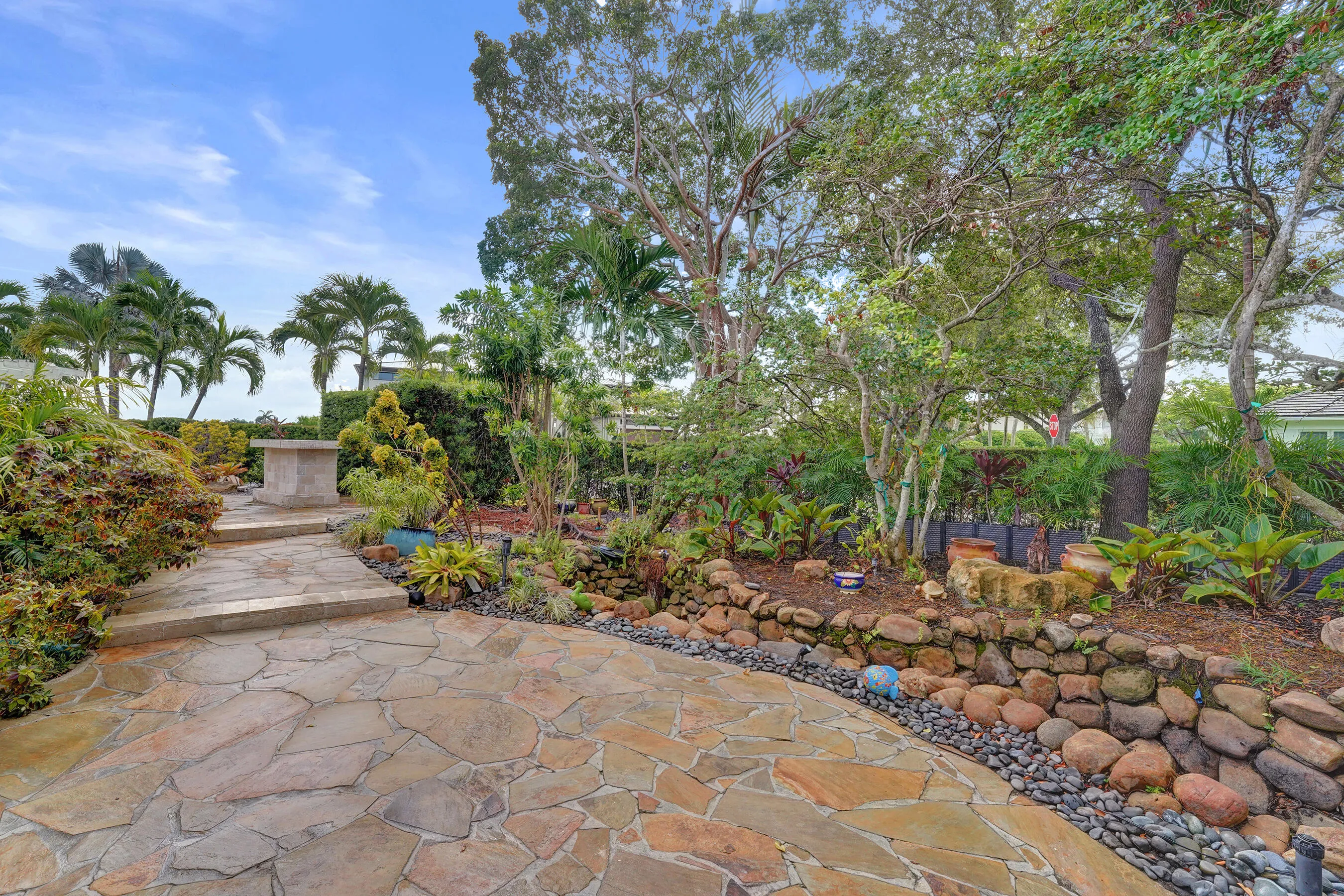 Expansive flagstone patio with a stone retaining wall, varied landscaping, and mature trees