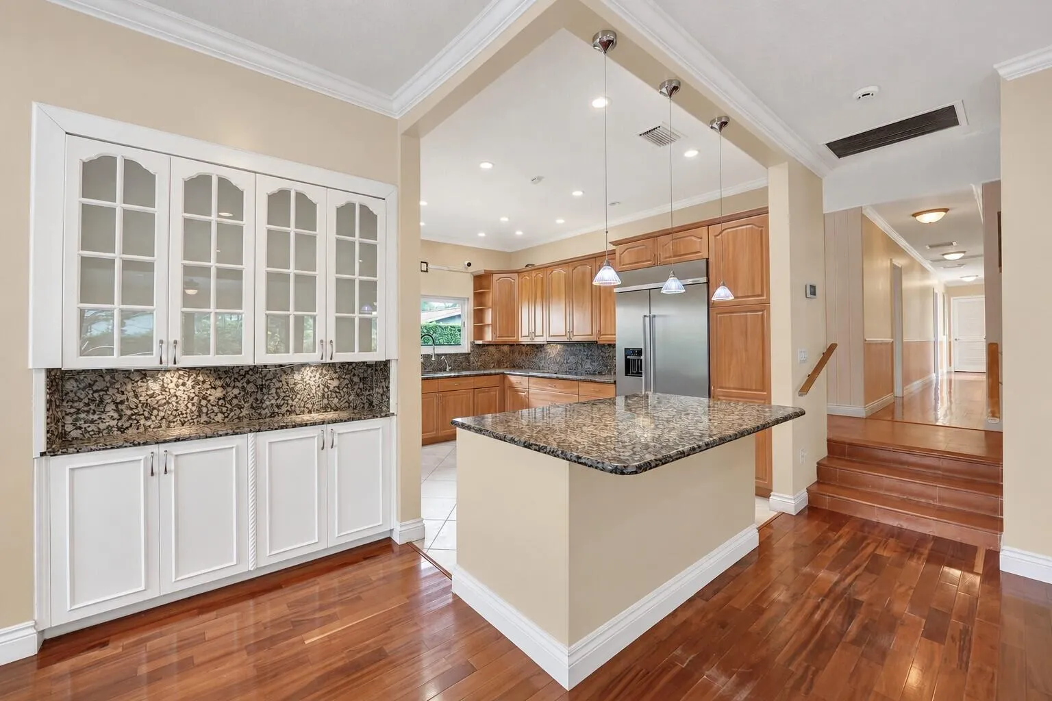 Wood flooring throughout, with a built-in white cabinetry unit featuring glass panel doors and under-cabinet lighting. Wall color has been virtually enhanced.