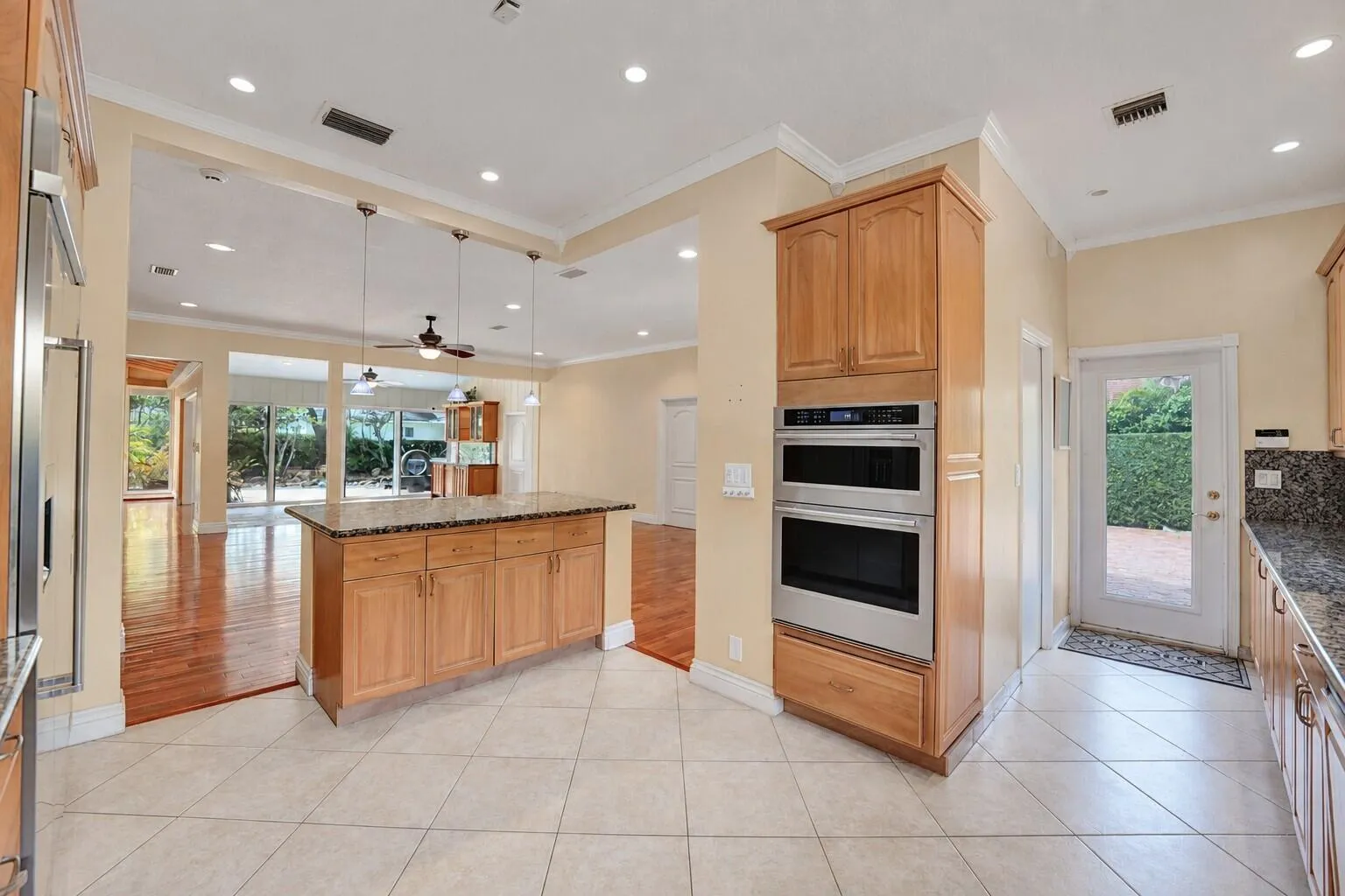 Kitchen featuring an island with granite countertops, built-in double ovens, light wood cabinetry, and recessed lighting. Wall color has been virtually enhanced.