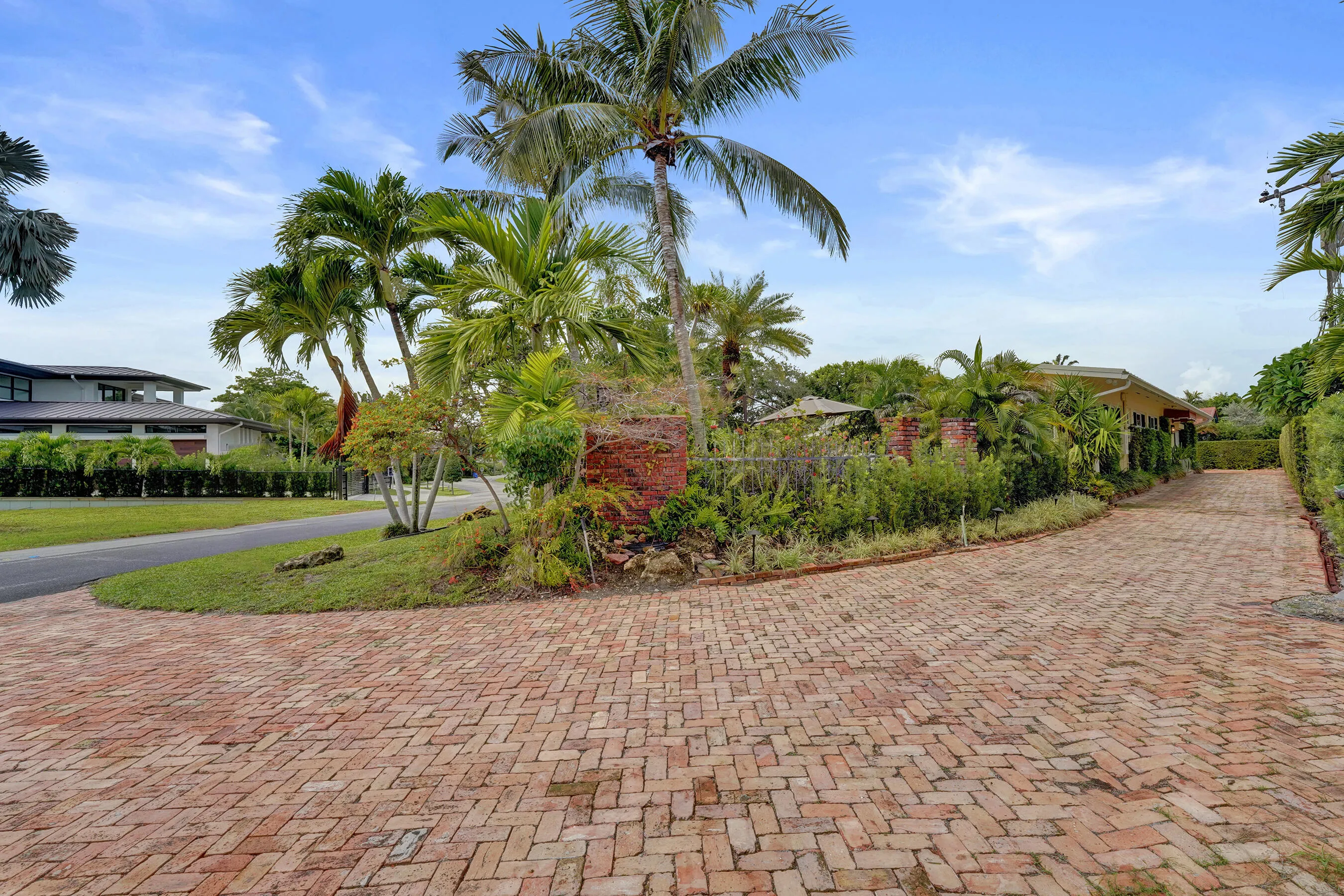 Extensive brick paver driveway with lush landscaping and mature palm trees