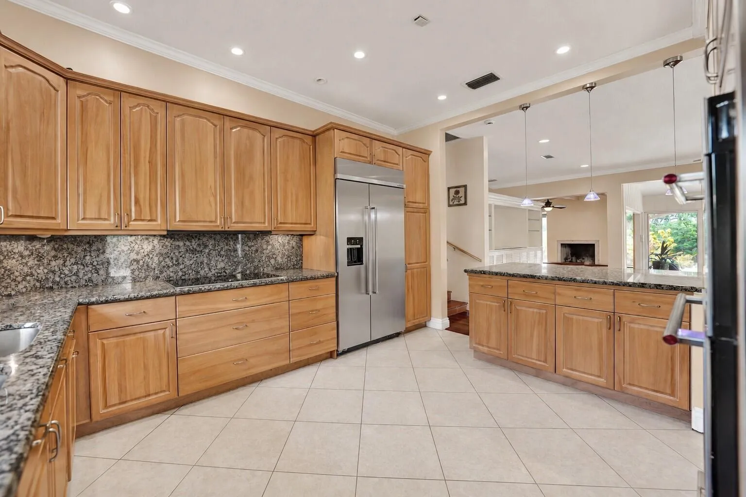 Ceramic tile flooring, light wood-finish cabinetry, stainless steel refrigerator, granite countertops, and recessed lighting. Wall color has been virtually enhanced.