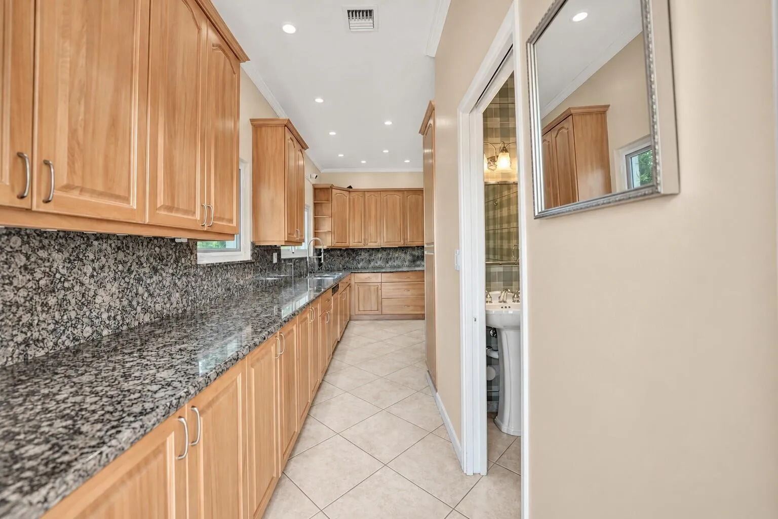 Extensive granite countertops with matching backsplash, light wood cabinetry, recessed lighting, and tile flooring. Wall color has been virtually enhanced.