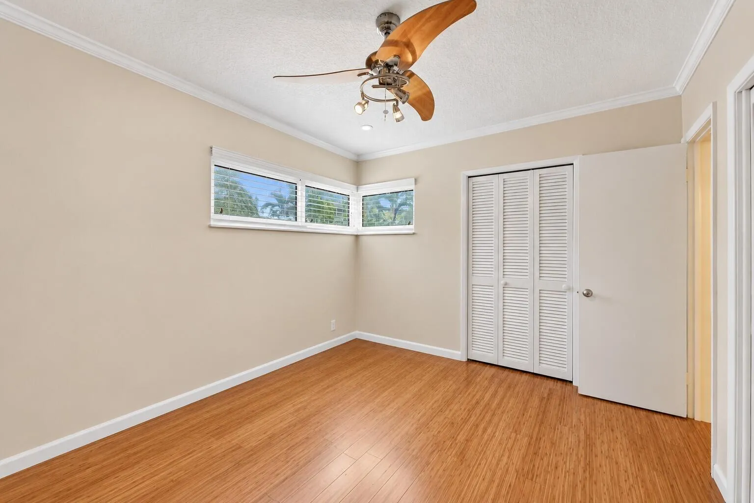 Wood-finish flooring, corner window configuration, bifold louvered closet doors, ceiling fan with integrated lighting, and crown molding