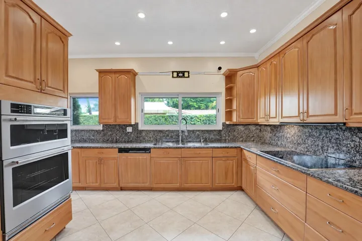 Kitchen featuring wood-finish cabinetry, stone countertops, integrated double oven, and recessed lighting. Wall color has been virtually enhanced.