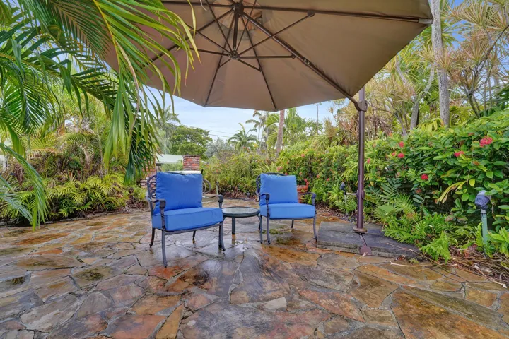 Stone patio with alcove sitting areas, an umbrella shade and lush tropical landscaping