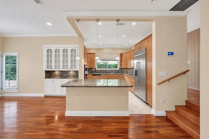 Wood-finish flooring throughout, kitchen with wood cabinetry and stainless steel appliances, breakfast bar with stone countertop, white built-in cabinetry with glass doors. Wall color has been virtually altered.