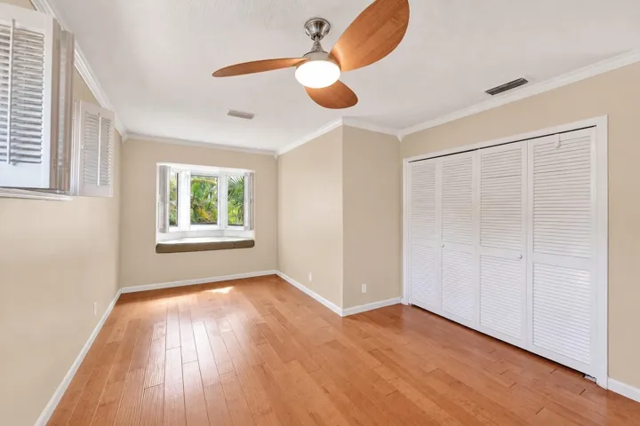 Hardwood flooring, bay window with integrated seating, white louvered bifold closet doors, crown molding, and ceiling fan with integrated lighting