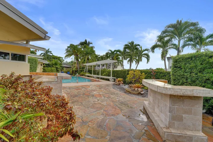 Outdoor space featuring a swimming pool, flagstone patio, built-in stone bar, and mature tropical landscaping