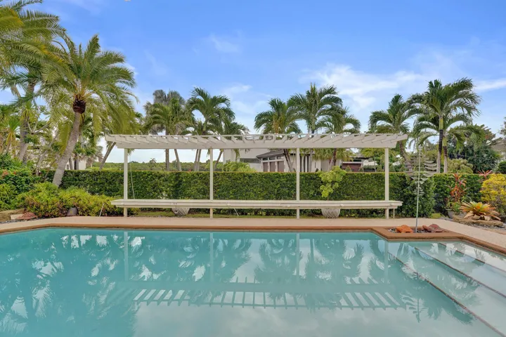Swimming pool with integrated steps, surrounded by a hardscaping border, a white pergola, and lush perimeter landscaping