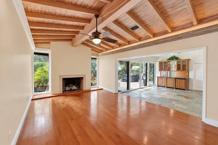 Exposed beam ceiling with wood paneling, wood-finish flooring, stone-clad fireplace, built-in cabinetry, and sliding glass doors