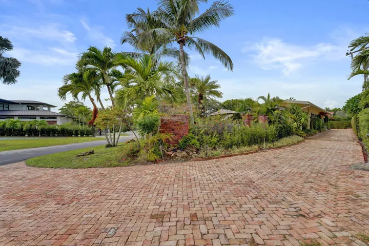 Extensive brick paver driveway with lush landscaping and mature palm trees