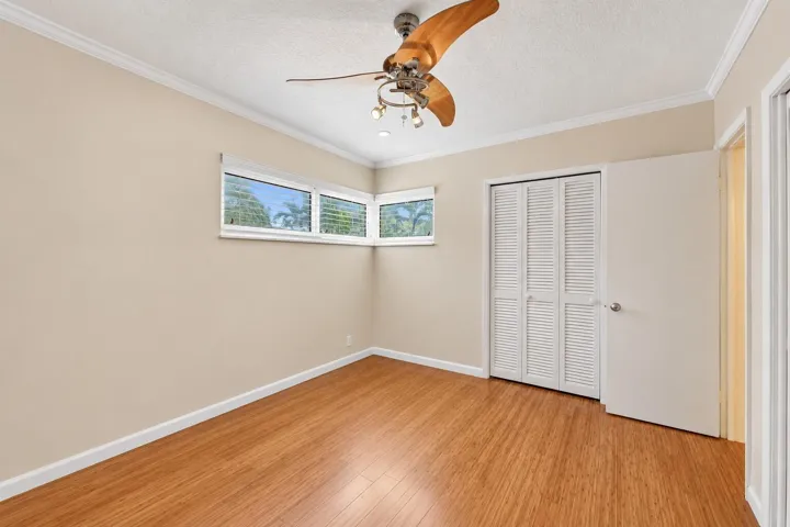 Wood-finish flooring, corner window configuration, bifold louvered closet doors, ceiling fan with integrated lighting, and crown molding