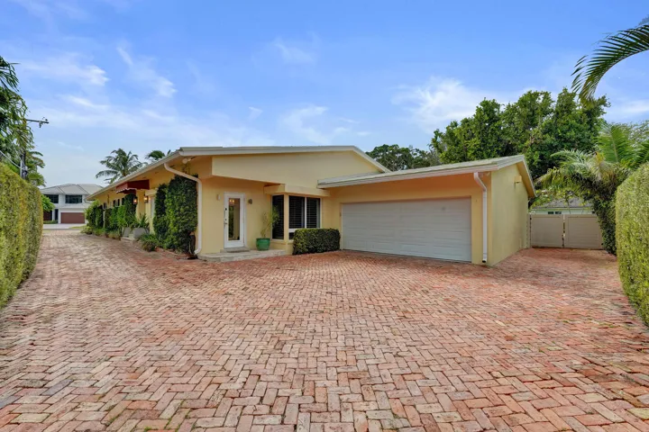 Driveway features plenty of space, leads to two-car garage, brick paver driveway, and mature landscaping.