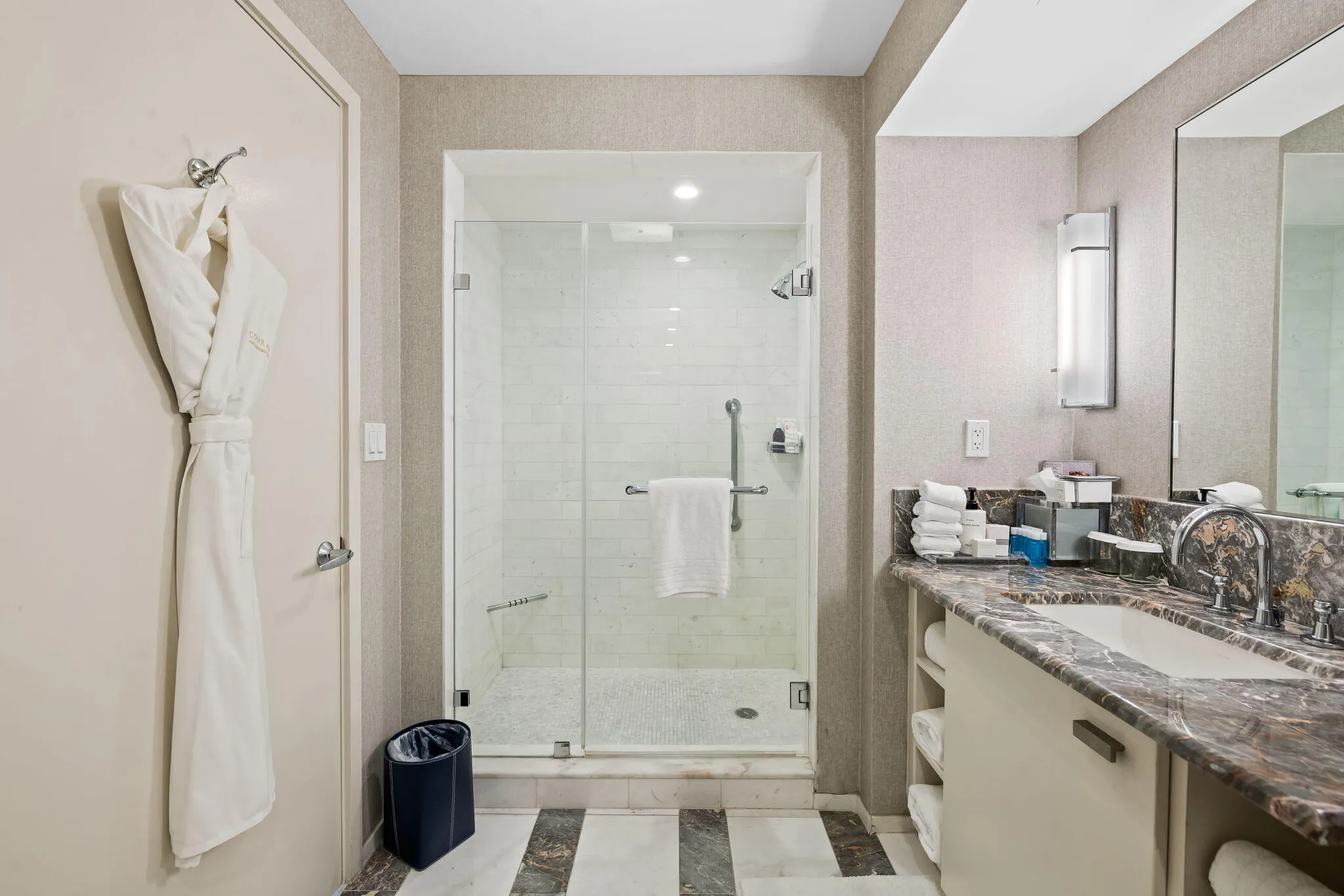 Glass-enclosed shower with subway tile, built-in vanity with stone countertop, under-mount sink, and wall-mounted lighting