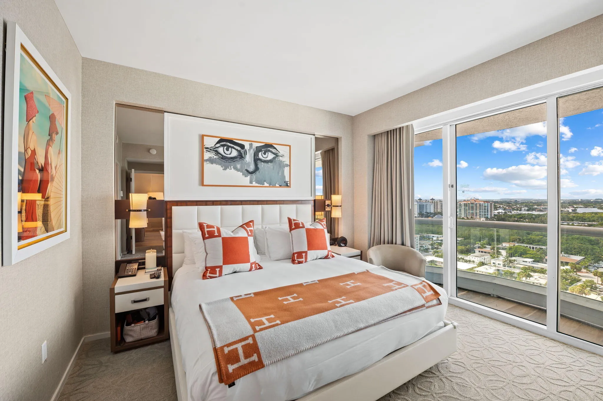 Sliding glass doors with balcony access, upholstered headboard, built-in bedside tables with storage, wall-mounted lighting fixtures, and textured wall coverings