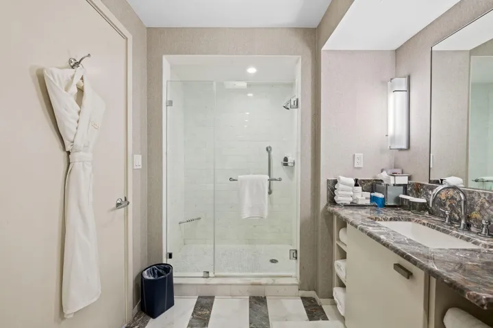 Glass-enclosed shower with subway tile, built-in vanity with stone countertop, under-mount sink, and wall-mounted lighting
