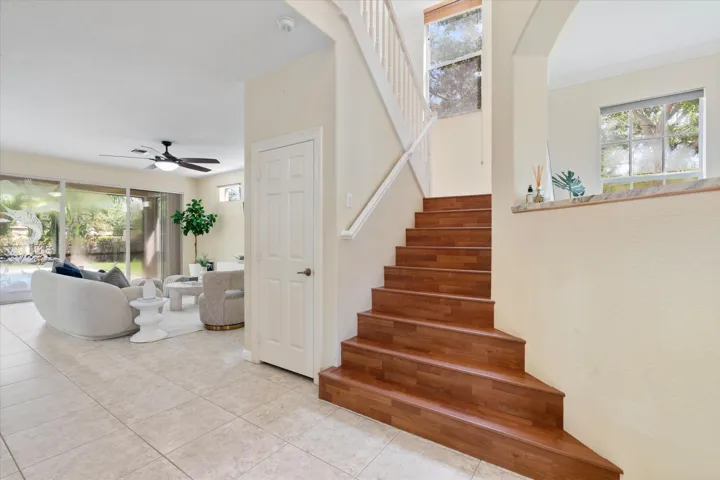 Wood-finish staircase with white risers, an open-concept living area with large format tile flooring, and sliding glass doors leading to an outdoor area