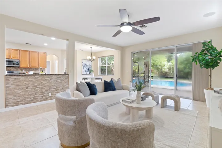 Open concept living area with light tile flooring, illuminated ceiling fan, and sliding glass doors leading to a private swimming pool