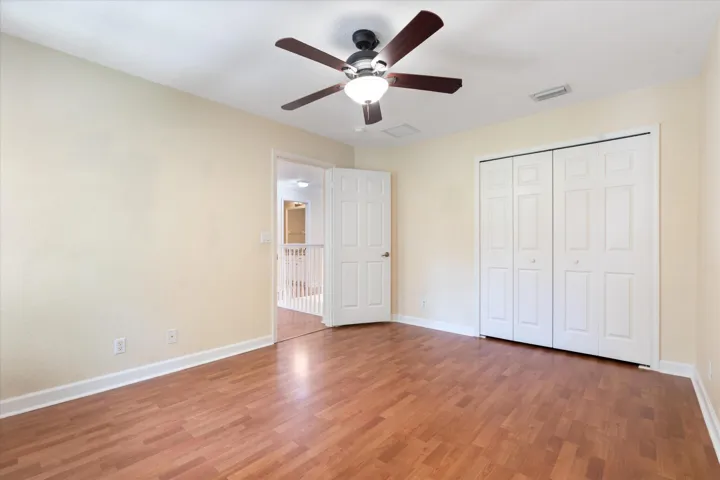 Wood-finish flooring with a ceiling fan, bifold closet doors, and a white interior door