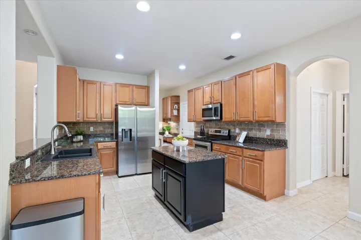 Kitchen featuring light wood-finish cabinetry, dark granite countertops, stainless steel appliances, a center island with additional storage, and tiled flooring