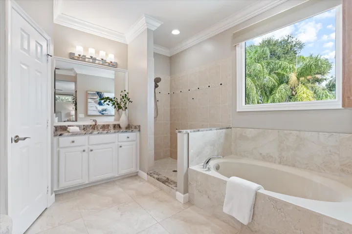 Tiled walk-in shower with a rain shower head, built-in soaking tub, a single vanity with a mounted mirror, wood-finish cabinetry, and a large window