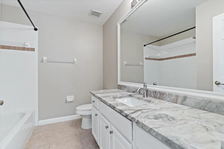 White tile shower with accent band, single white vanity with undermount sink, stone-finish countertop, and full-width wall mirror