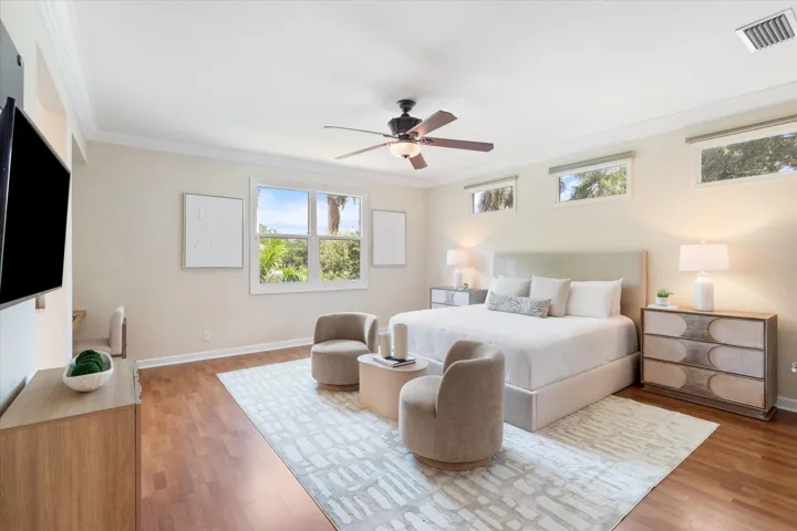 Spacious room featuring wood-finish flooring, multiple windows, a ceiling fan, and crown molding