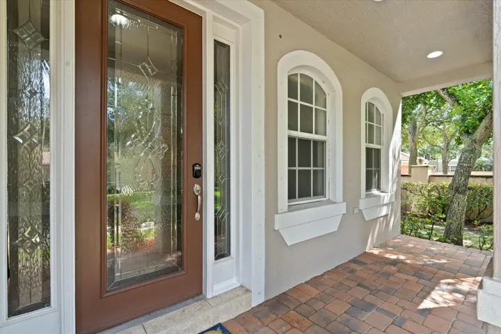 Entryway featuring a decorative glass door, sidelights, arched windows with white trim, recessed lighting, and brick paver flooring