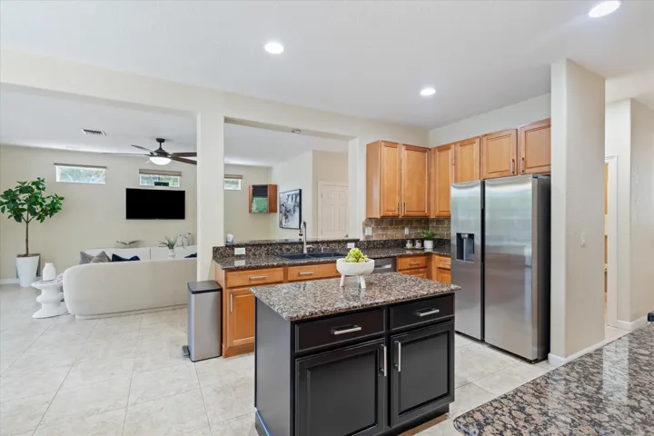 Kitchen featuring a central island with dark cabinetry, granite countertops, tile flooring, stainless steel appliances, and wood-finish cabinetry