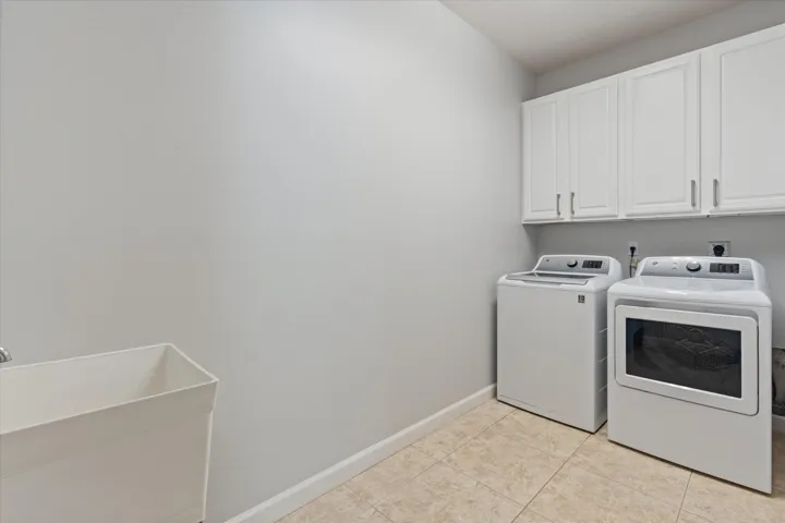 Utility room featuring upper cabinetry, a utility sink, and tiled flooring