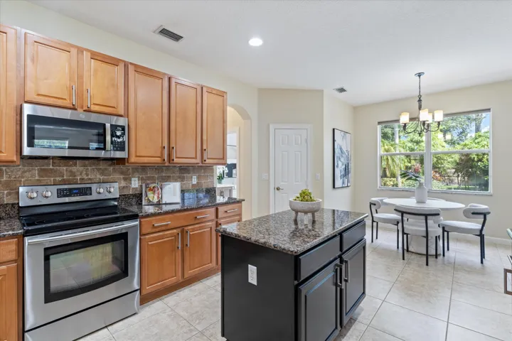 Kitchen featuring stainless steel appliances, wood-finish cabinetry, a stone-finish backsplash, and an island with a stone-finish countertop