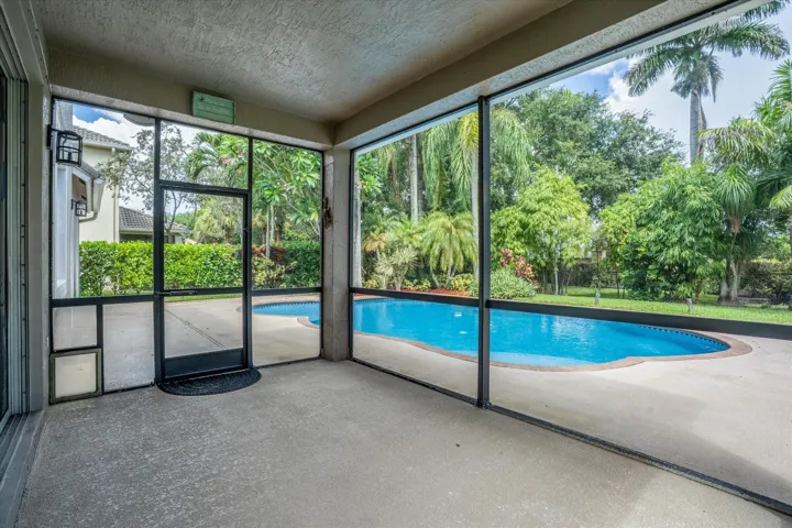 Expansive screened patio with a concrete surface, providing access to a free-form swimming pool, concrete pool deck, and lush landscaping