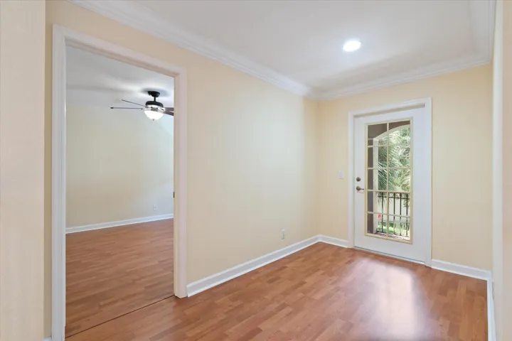 Wood-finish flooring throughout, crown molding, recessed lighting, and a French door with transom window leading to a balcony